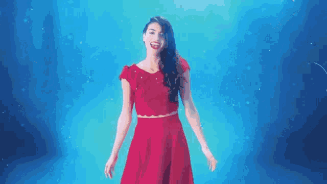 a woman in a red dress is standing in front of a blue background and smiling .