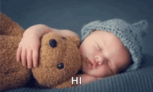 a baby sleeping with a teddy bear that says hi on the bottom
