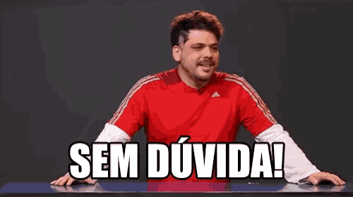 a man in a red shirt is sitting at a table with the words sem duda written on it .