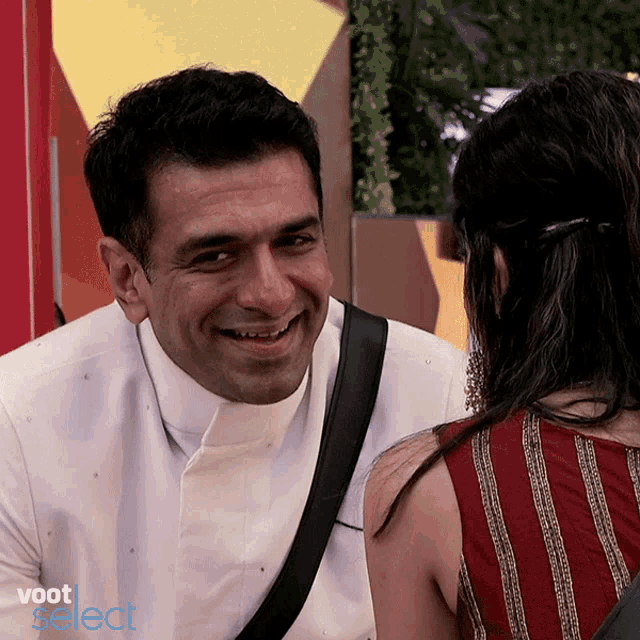 a man in a white shirt is smiling while looking at a woman in a red top with the words voot select below him