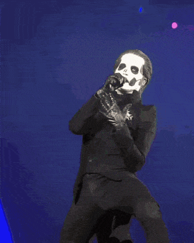 a man in a ghost mask is singing into a microphone on stage .