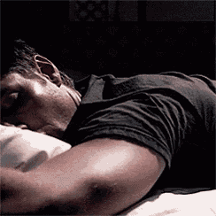 a man in a black shirt is laying on a bed with his head on a pillow .