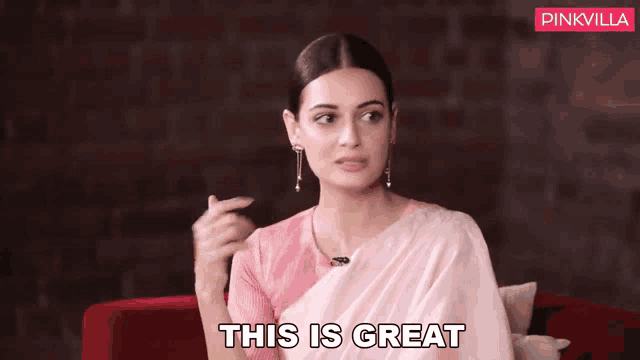 a woman in a pink saree is sitting on a red couch and says this is great .