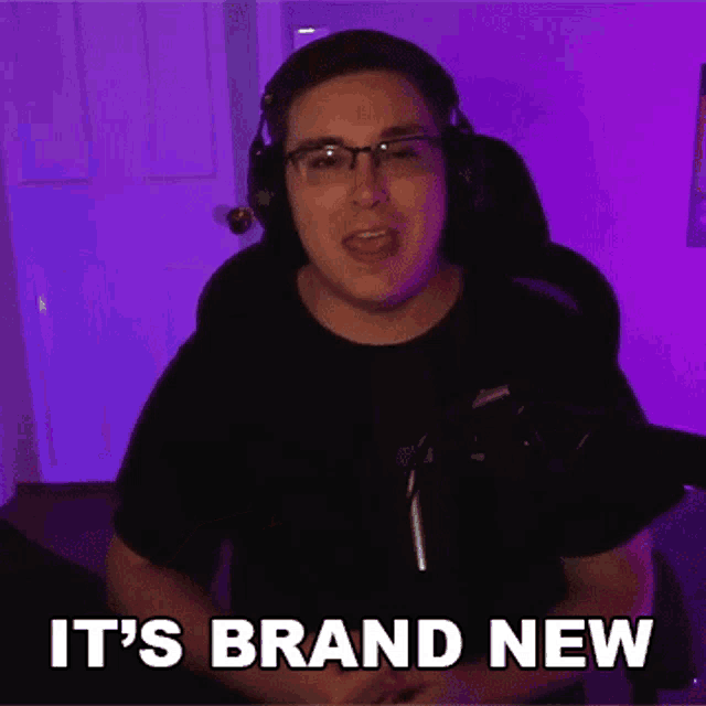 a man wearing headphones and glasses is sitting in front of a microphone and says it 's brand new .