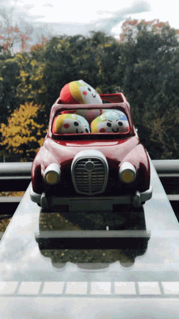 a red toy car with two clown dolls in it