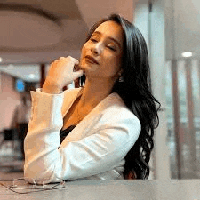 a woman in a white jacket is sitting at a counter with her hand on her chin .
