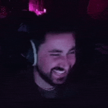 a man with a beard is wearing headphones and smiling while sitting in front of a computer screen .