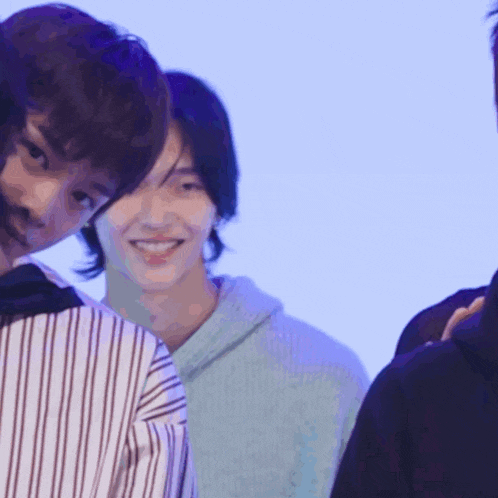 a man in a blue sweater smiles while standing next to two other men