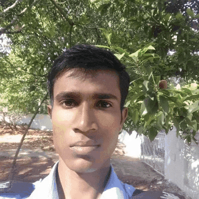 a man in a blue shirt is taking a selfie in front of trees