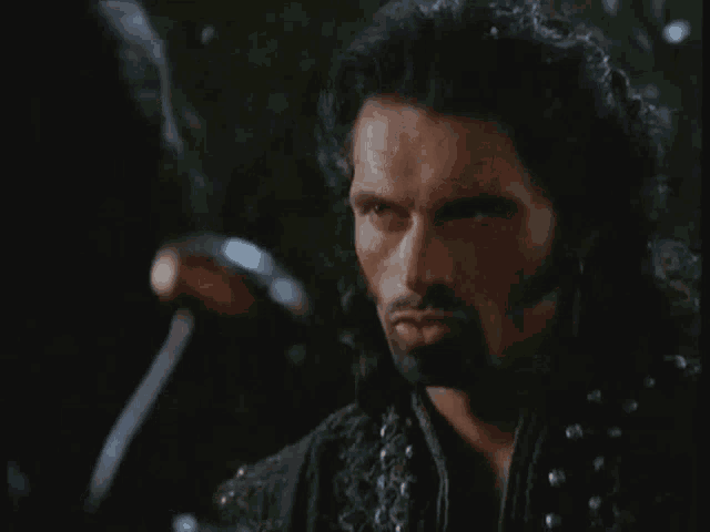 a man with a beard is holding a sword and says " so "