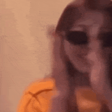 a woman wearing sunglasses and an orange shirt is covering her mouth with her hand .