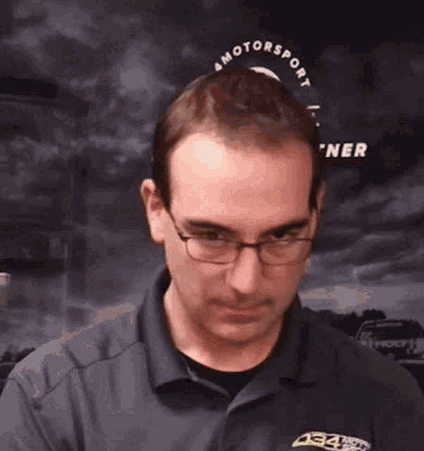 a man wearing glasses and a motorsport shirt