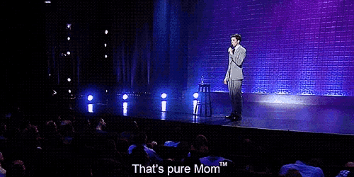a man stands on a stage holding a microphone and says " that 's pure mom "