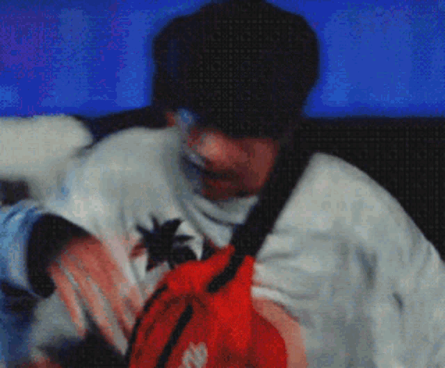 a man wearing a white shirt with a palm tree on it is holding a red supreme bag