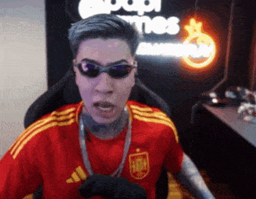 a man wearing sunglasses and a red adidas shirt is sitting in a chair
