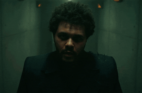 a man with a beard and curly hair is standing in a dark room