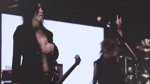 a man playing a guitar in front of a microphone while another man stands behind him