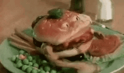 a hamburger with a face on it is on a plate with peas and vegetables .