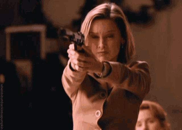 a woman in a brown jacket is pointing a gun at the camera with a caption that starts with the word up