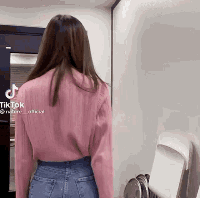 a woman wearing a pink shirt and blue jeans is standing in front of a door .