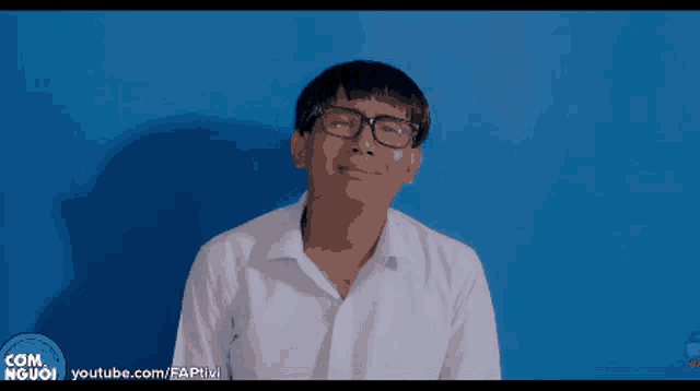 a man wearing glasses and a white shirt is standing in front of a blue wall and a youtube logo