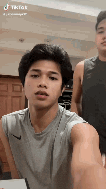 a man in a grey nike tank top takes a selfie next to another man