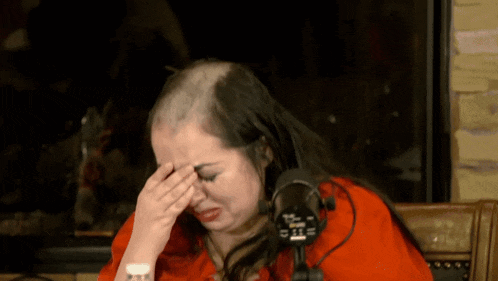a woman with a shaved head is crying in front of a microphone