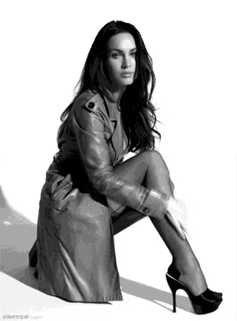 a woman in a trench coat and high heels is sitting down