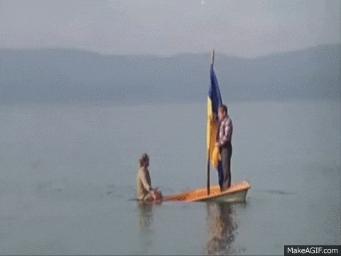 a man is standing on a boat with a flag in the water .