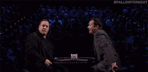 two men are standing next to each other in a dark room with their mouths open and their hands in the air .