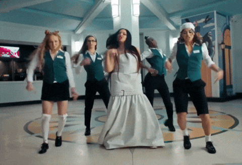 a woman in a white dress is dancing with a group of women in green vests