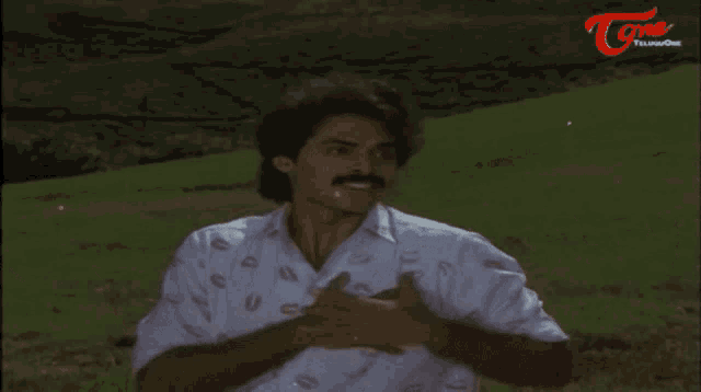 a man wearing a shirt with kisses on it is standing in a field