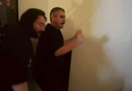 a man with a mustache is standing next to another man in a dark room