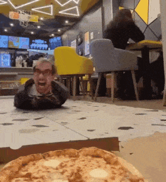 a man laying on the floor in a restaurant with a pizza in the foreground