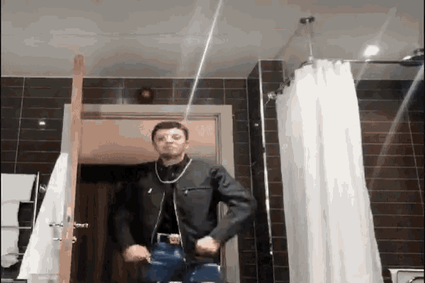 a man in a black jacket is standing in a bathroom with a shower curtain .