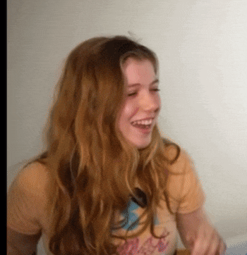 a woman with long red hair is smiling and wearing a yellow shirt that says ' california ' on it