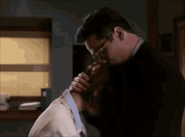 a man with glasses is kissing a woman on the neck in a room .