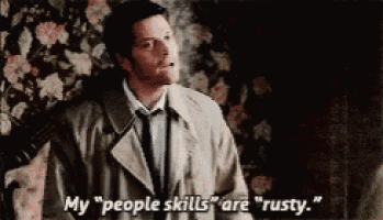 a man in a trench coat and tie is smoking a cigarette and saying " my people skills are rusty "