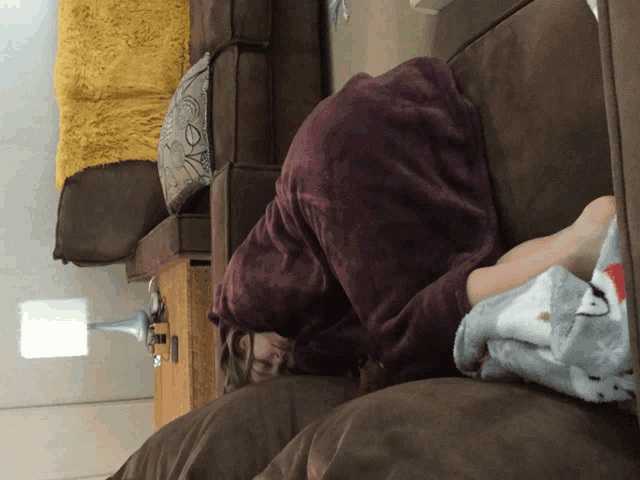 a person laying on a couch with a purple blanket
