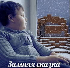 a boy in a grey sweater is looking out a window while snow falls