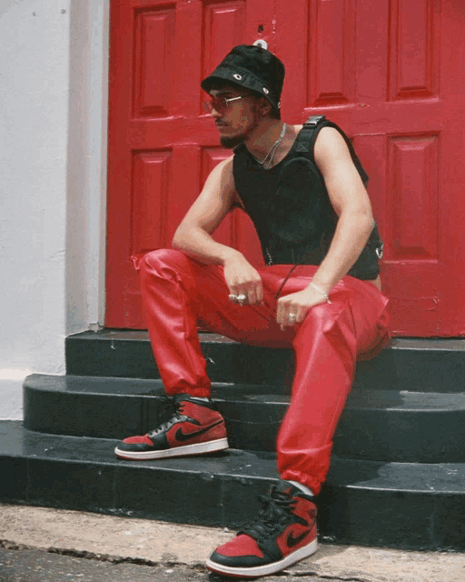 a man wearing red pants and a black hat sits on a set of steps