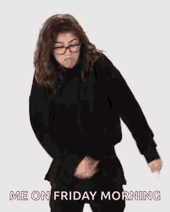 a woman wearing glasses and a black sweater is dancing in front of a white background .