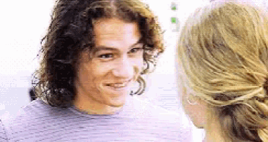 a man with long curly hair is smiling at a woman with blonde hair .