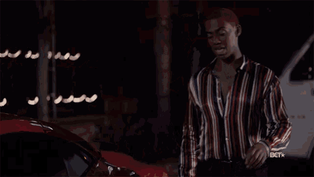 a man in a striped shirt stands in front of a red car with the betx logo on the bottom