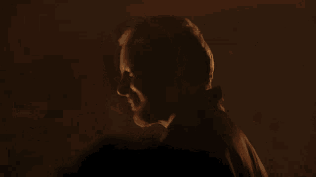 a man with a beard is standing in a dark room and looking down .