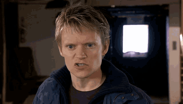 a man wearing a blue jacket and a purple shirt looks at the camera