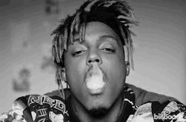 a black and white photo of a man blowing a bubble while smoking a cigarette .