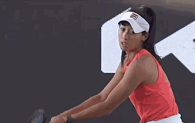 a woman is swinging a tennis racket at a tennis ball while wearing a visor .