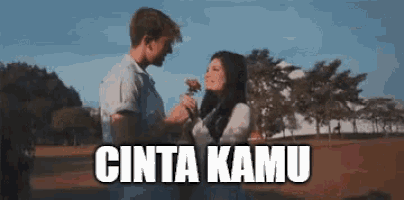 a man is giving a flower to a woman in a field with the words cinta kamu written below them .