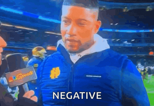 a man wearing a blue jacket is talking into a microphone and the word negative is on the screen .